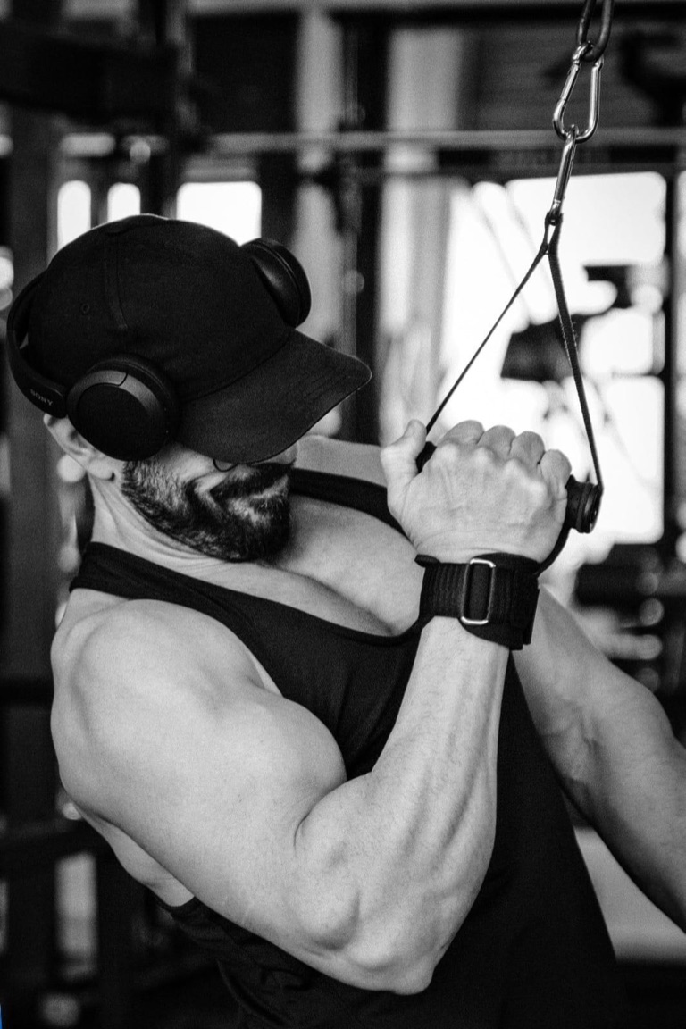 Alejandro Albornoz entrenando en polea, gorra y auriculares, brazo en tensión.