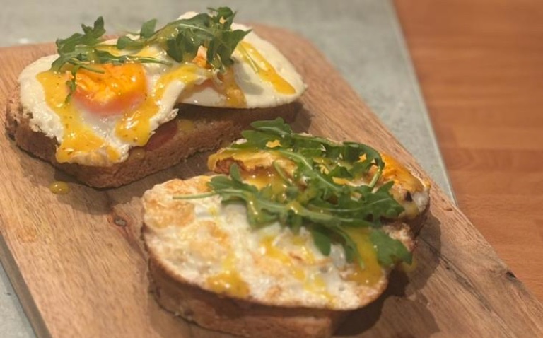 Dos tostadas de pan de masa madre con huevo y rúcula sobre una tabla de madera.