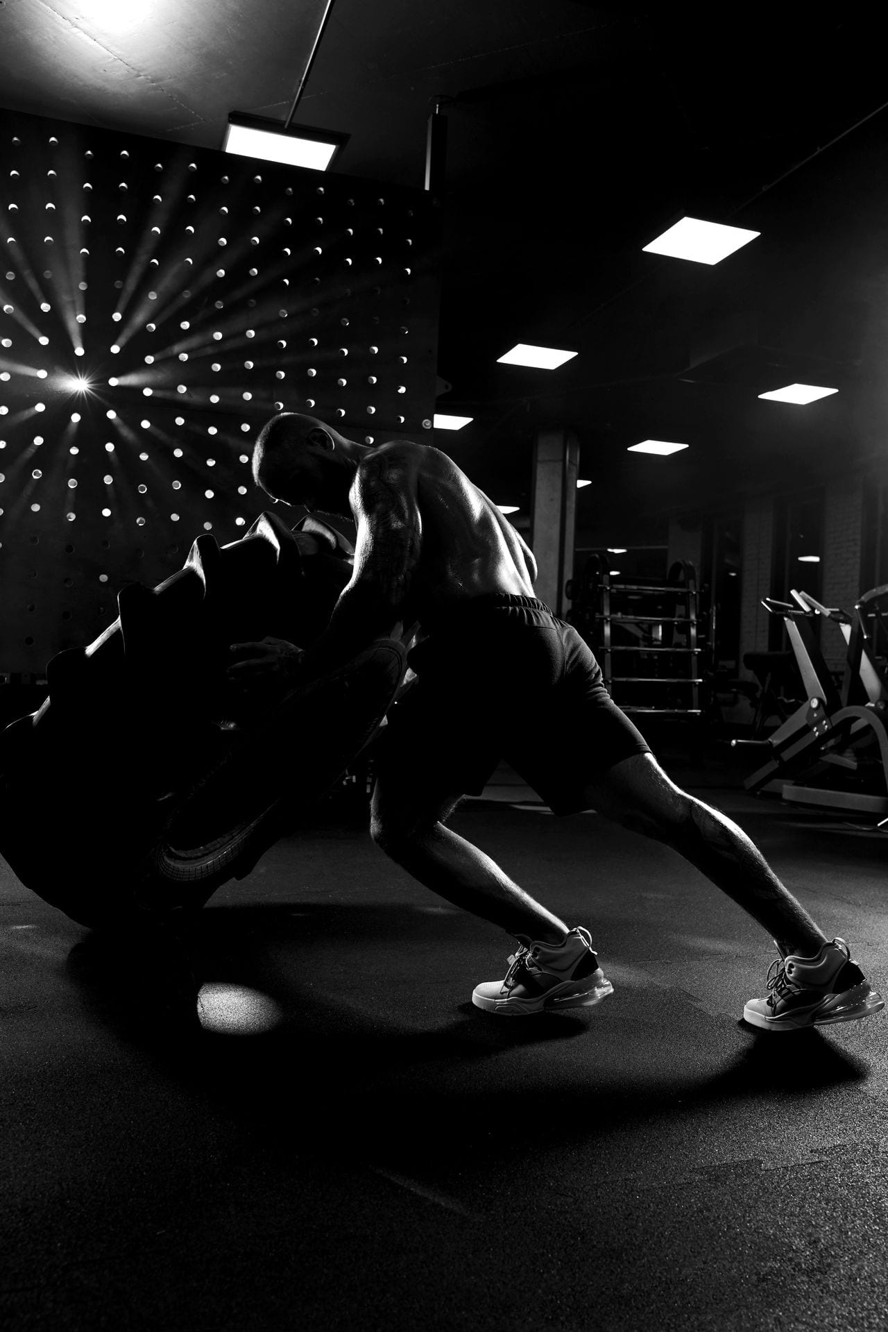 Atleta volteando un neumático gigante en un gimnasio en penumbra.